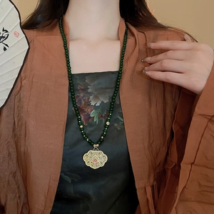Close-up of emerald green beaded necklace with golden filigree pendant on a model