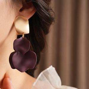 Close-up of a model wearing irregular gold metal earrings with deep purple matte petals