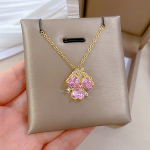 Detail of hand holding gold necklace with three pink heart-shaped crystal petals