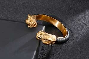 Detailed view of golden dragon head bangles with black leather texture on dark background