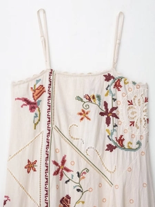 Detail of floral embroidery and geometric cutouts on off-white linen dress fabric