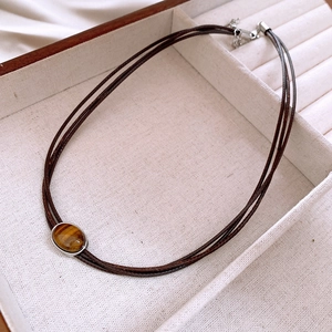 Detailed view of an oval tiger eye stone pendant on a triple-strand brown cord necklace