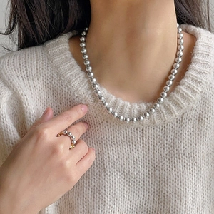 Detail of grey pearl necklace and gold multi-pearl ring on a beige knitted sweater
