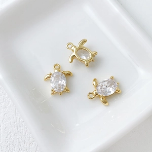 Detailed view of three 14k gold-plated turtle charms with oval cubic zirconia in ceramic tray