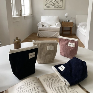 Set of four corduroy makeup bags in black, beige, pink and blue on a cozy sofa