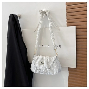 Detail view of the white textured cloud bag with a floral chain and pleated fabric strap