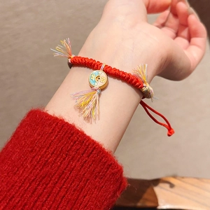 Gros plan d'un bracelet en corde tressée rouge avec breloque dorée Ruyi et pompons colorés