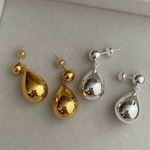 Detail view of gold and silver teardrop earrings with polished finish on gray felt