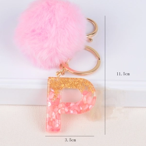 Close-up of a pink resin letter P keychain with gold foil, plush pompom and dimensions