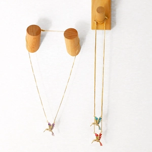 Vue macro détaillée de pendentifs colibri en émail coloré sur de fines chaînes dorées