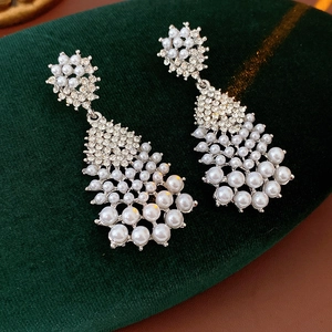 Close-up of silver drop earrings with pearls and crystals on green velvet surface