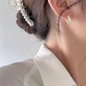 Detail of twisted silver earrings and a white pearl hair claw clip worn by a model