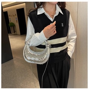 Detail of silver metallic woven handbag held by a model wearing a black knitted vest