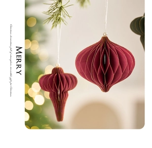 Detail of red honeycomb paper ornament with gold edges and pearl hanging on Christmas tree