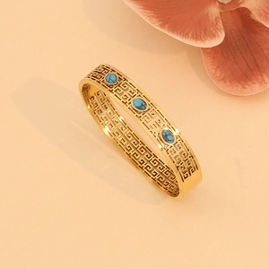Close-up of golden hollow-out bangle with turquoise stones and floral accents