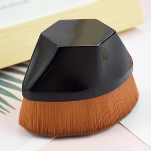 Hexagonal black handle makeup brush with dense orange-brown bristles on a white desk