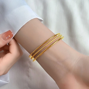 Three-piece gold bangle set featuring matte and polished finishes on a woman's wrist