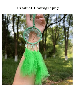 Detail of tree of life dreamcatcher with green feathers held against nature background