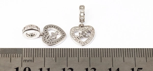 Macro view of silver heart charms with Mom engraving and zircon inlay near a ruler