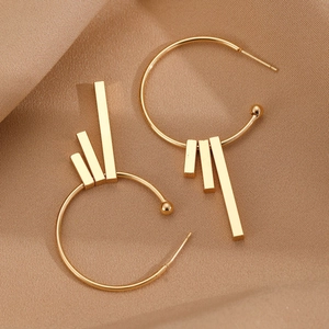 Detailed macro view of large gold geometric hoop earrings with metal bar charms on satin