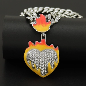 Detailed view of silver Cuban chain with rhinestone heart and yellow flame pendant