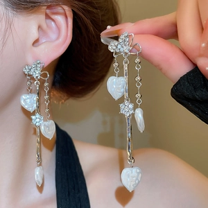 Détail de boucles d'oreilles pompons cœur avec aiguilles en argent papillon et cristaux