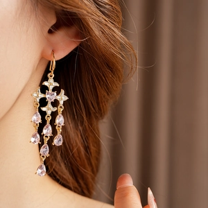 Detail of gold cross earring featuring pink teardrop crystals on model with soft backdrop