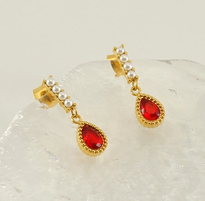 Macro view of gold teardrop earrings with red crystal and white pearl studs on ice