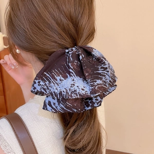 Rear view of model wearing a large brown fabric claw clip with blue abstract ink patterns