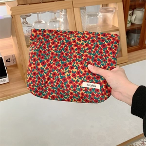 Gros plan d'une pochette fleurie en velours côtelé tenue à la main montrant sa taille