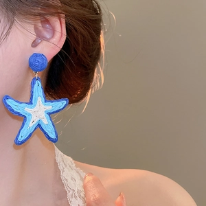 Detail showing handwoven raffia starfish earring in blue and white on model