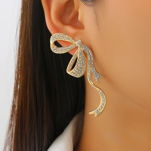 Detalle de elegantes pendientes de lazo dorado con brillantes de imitación incrustados