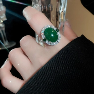 Détail d'une bague en agate verte avec zircons portée par un mannequin tenant un verre