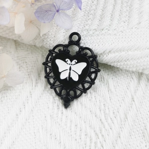 Detail of heart-shaped alloy pendant with white butterfly enamel and hollow-out design