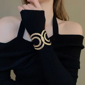 Minimalist wide gold crossover cuff bracelet with textured rope design over a black sleeve