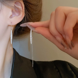 Close-up of long silver tassel earrings with sparkling zircon stones worn by a model
