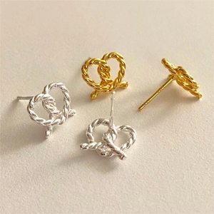 Detailed view of twisted heart-shaped stud earrings in gold and silver finishes
