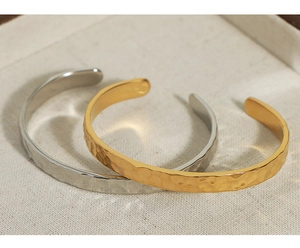 Dettaglio della trama martellata sui bracciali rigidi in acciaio al titanio oro e argento
