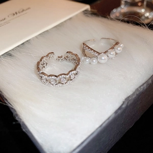 Macro detail of silver pearl and zircon crossover rings on soft plush background