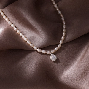 Detailed macro view of seed pearl necklace with a teardrop zircon pendant on brown silk