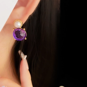 Gros plan sur une boucle d'oreille vintage en or avec perle blanche et pierre violette