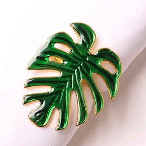 Green monstera leaf napkin ring with golden metal edges and enamel finish on white fabric