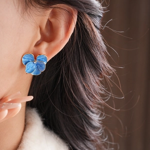 Gros plan sur une boucle d'oreille fleur en émail bleu avec bords dorés sur l'oreille
