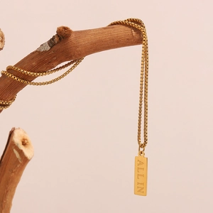 Detail of 18K gold-plated square pendant necklace with ALL IN engraving on a branch