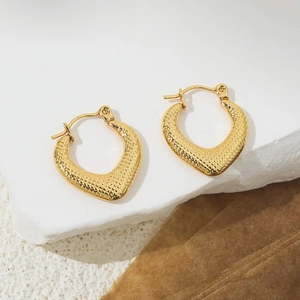 Close-up of 18K gold-plated heart hoop earrings with textured finish on a stone surface