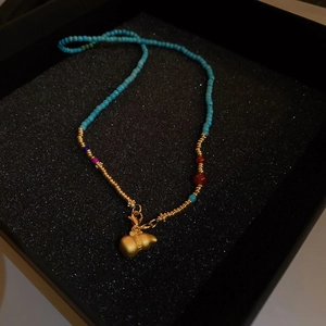 Détail du collier en perles bleu-vert avec pendentif gourde dorée sur fond noir