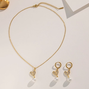 Close-up of golden heart pendant necklace and earrings with zircon and pearl details