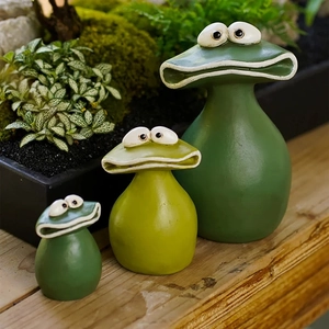 Lot de trois figurines de jardin grenouilles en résine verte sur une table en bois