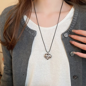 Detail of leopard print heart pendant necklace with black cord on model wearing cardigan