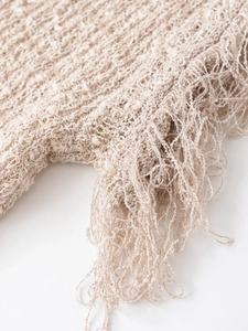 Macro detail of beige crochet knit vest showing hollow texture and tassel hem design